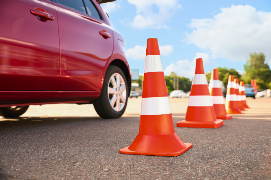 A red car maneuvers around orange traffic cones